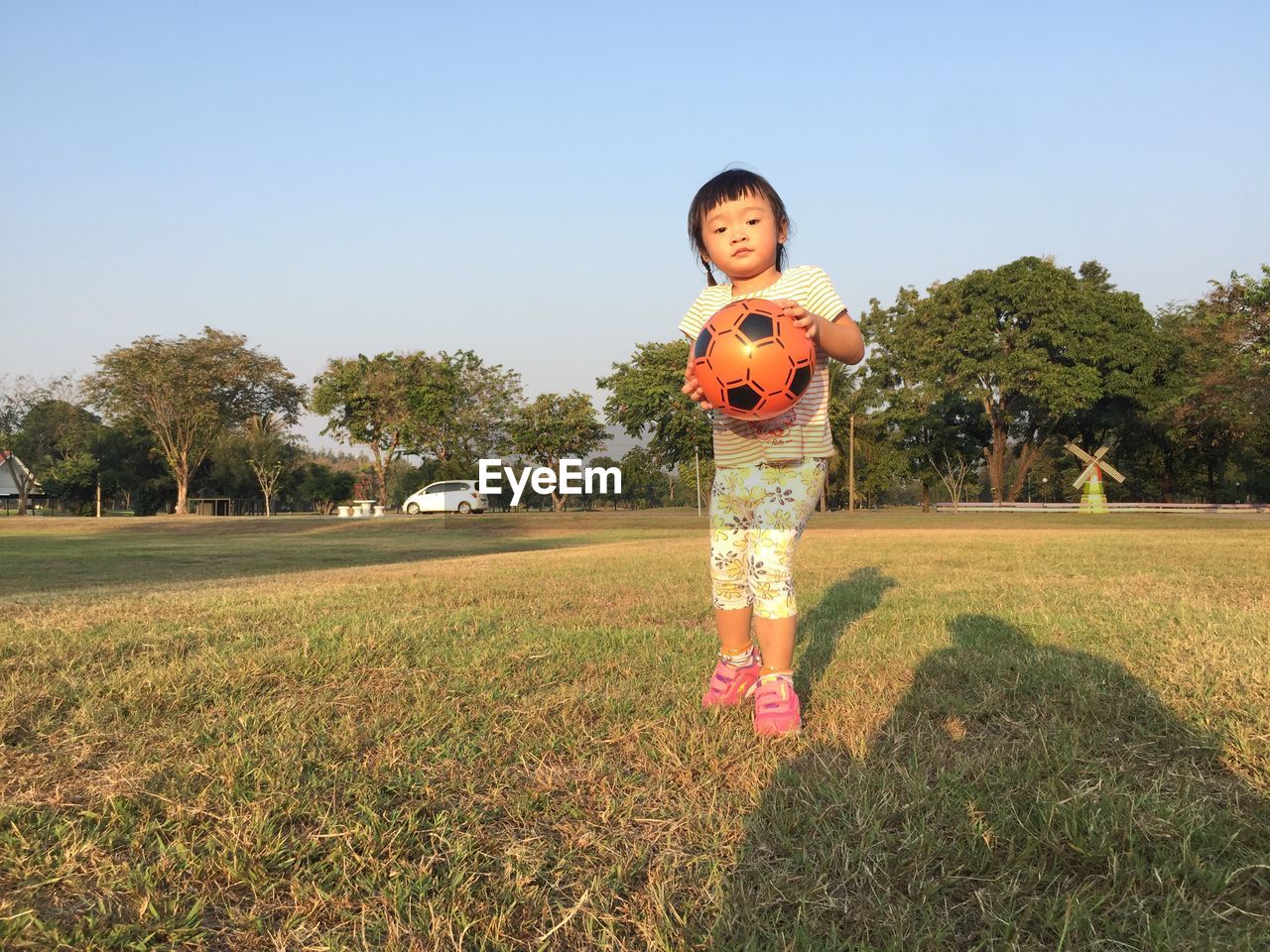 PORTRAIT OF SMILING GIRL STANDING ON FIELD AGAINST CLEAR SKY