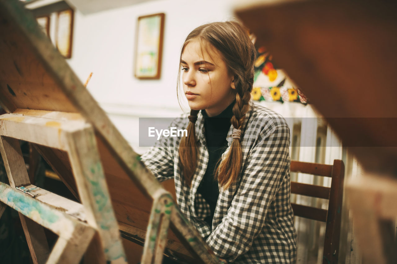 Art school, creativity and people concept - woman with easel, palette and brush painting at studio