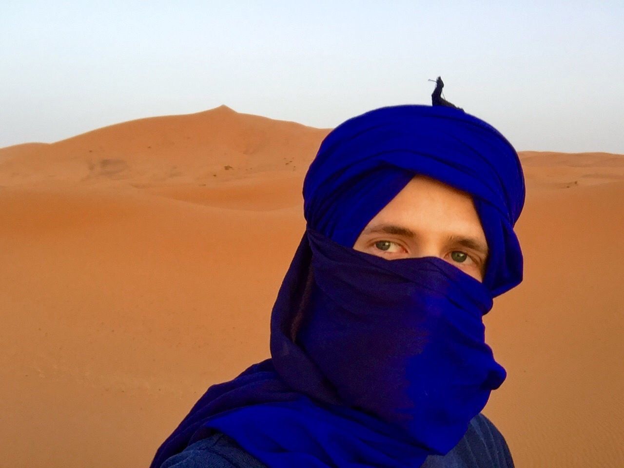 Close-up of man with blue headscarf at sahara desert against sky