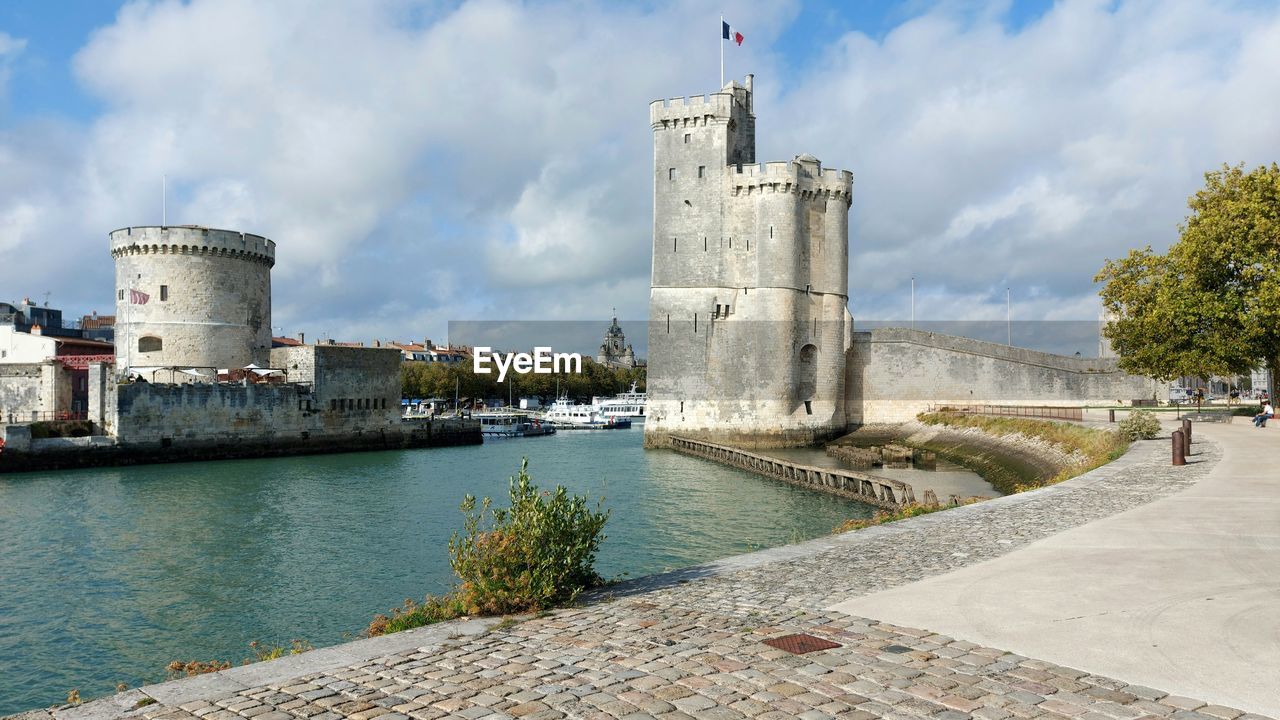 architecture, built structure, water, sky, building exterior, tower, cloud, nature, history, the past, sea, travel destinations, waterway, building, château, fortification, castle, day, landmark, coast, lighthouse, travel, fort, vacation, city, no people, outdoors, tourism, moat, wall, tree, blue