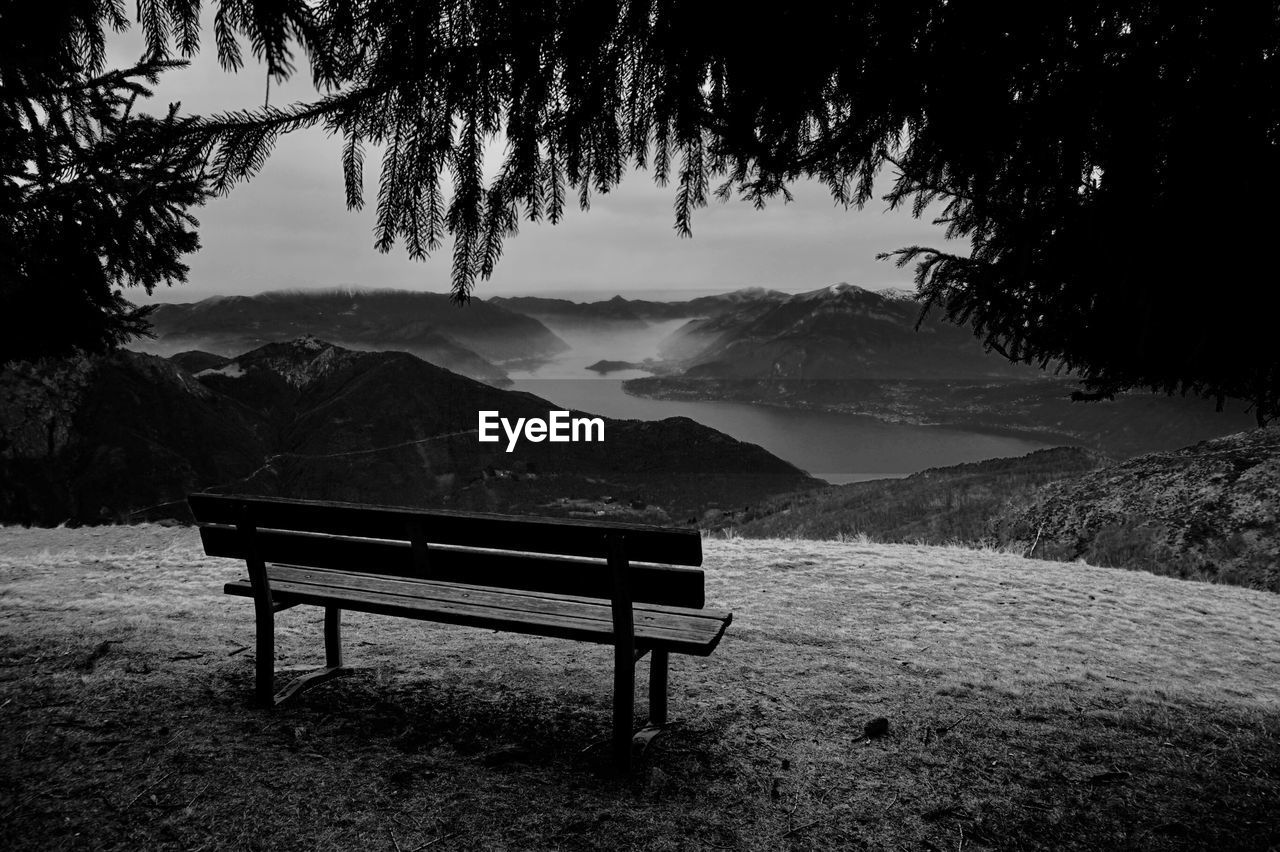Empty bench by mountains against sky in black and white