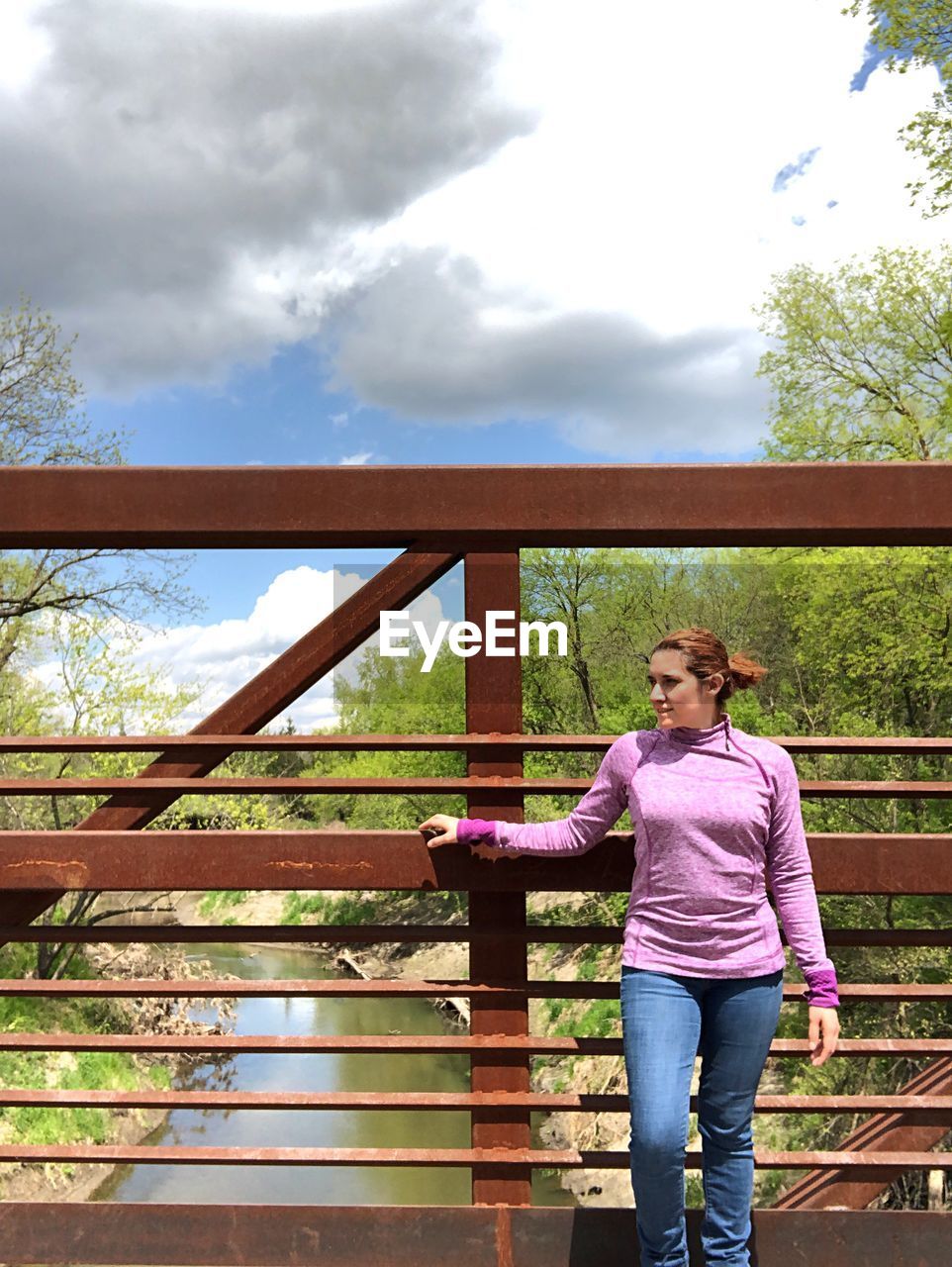 Young woman looking away while standing against railing on bridge