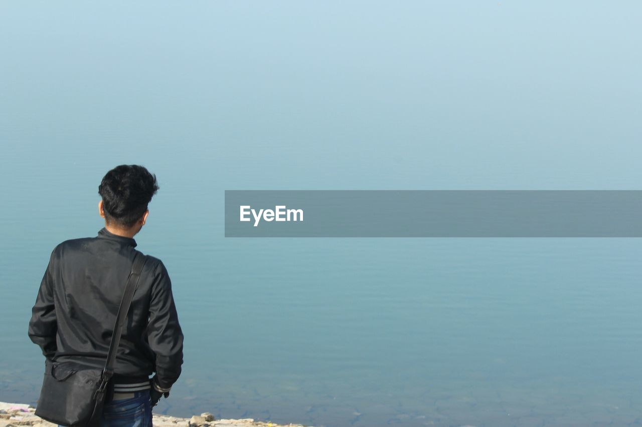 Rear view of young man standing on lakeshore