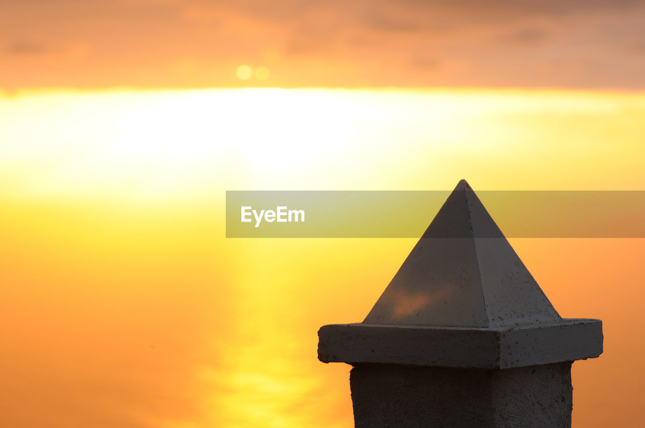 High section of built structure against sea during sunset