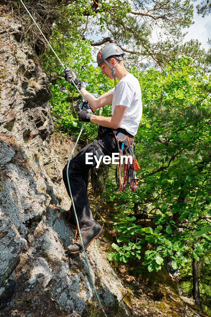 Full length of boy climbing on rock in forest