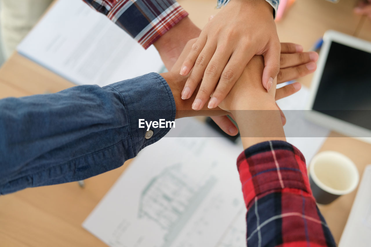 High angle view of cropped hands stacking over table at office