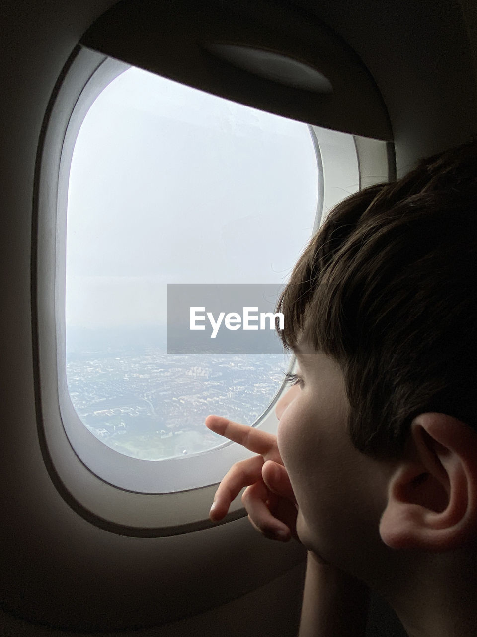 Opening of borders concept. kid looks and points to the landscape from the window of a flying plane.