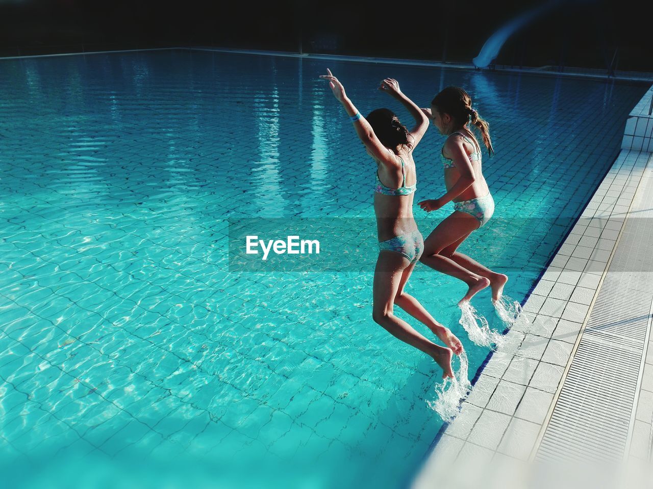 Full length of siblings in bikini jumping into swimming pool