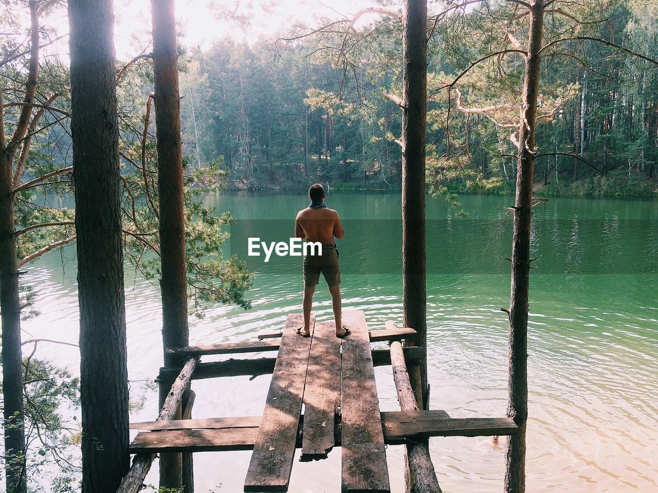 REAR VIEW OF MAN STANDING IN LAKE AGAINST TREES