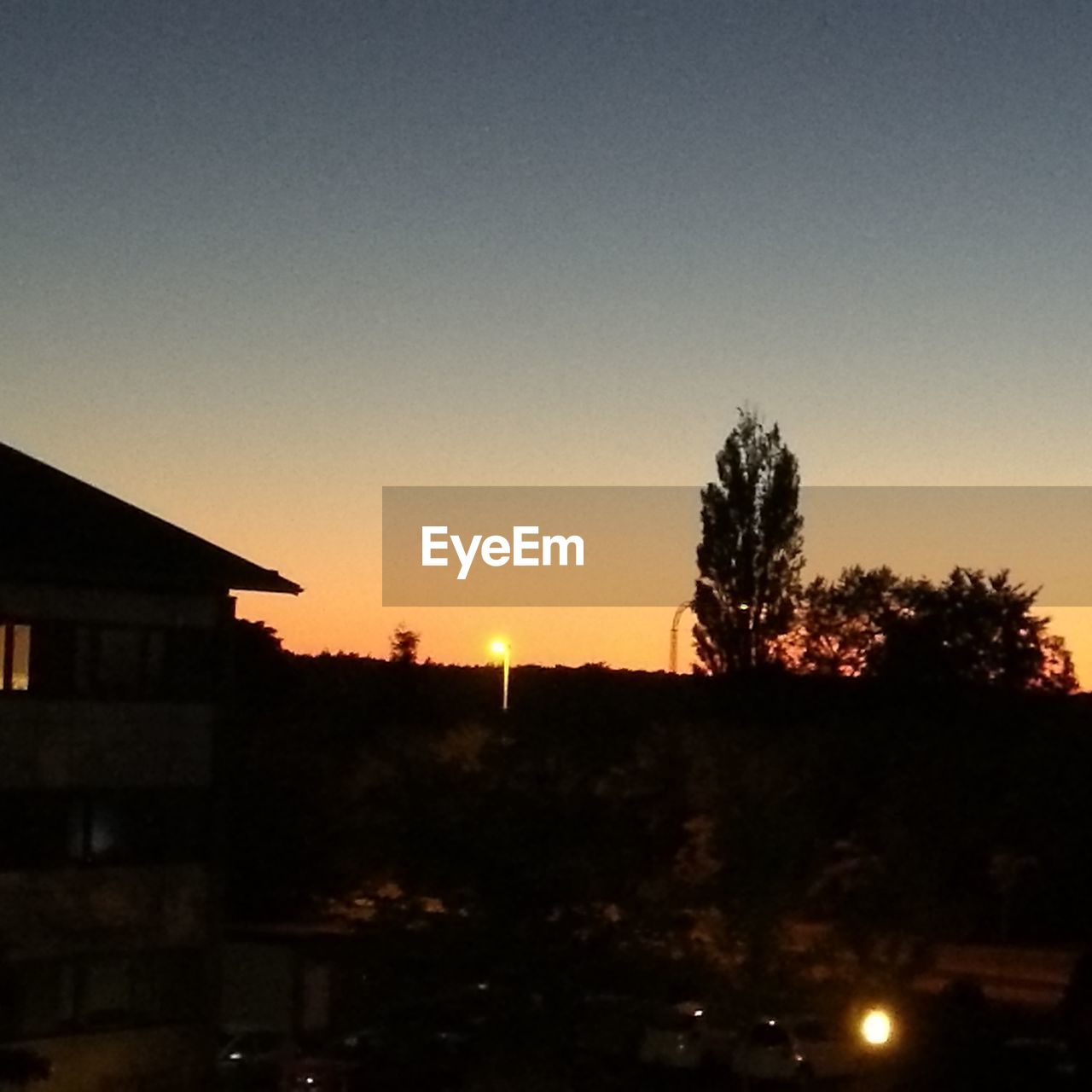 SILHOUETTE TREES BY BUILDING AGAINST SKY DURING SUNSET