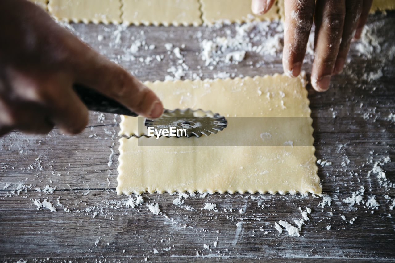 Cropped hands cutting ravioli dough
