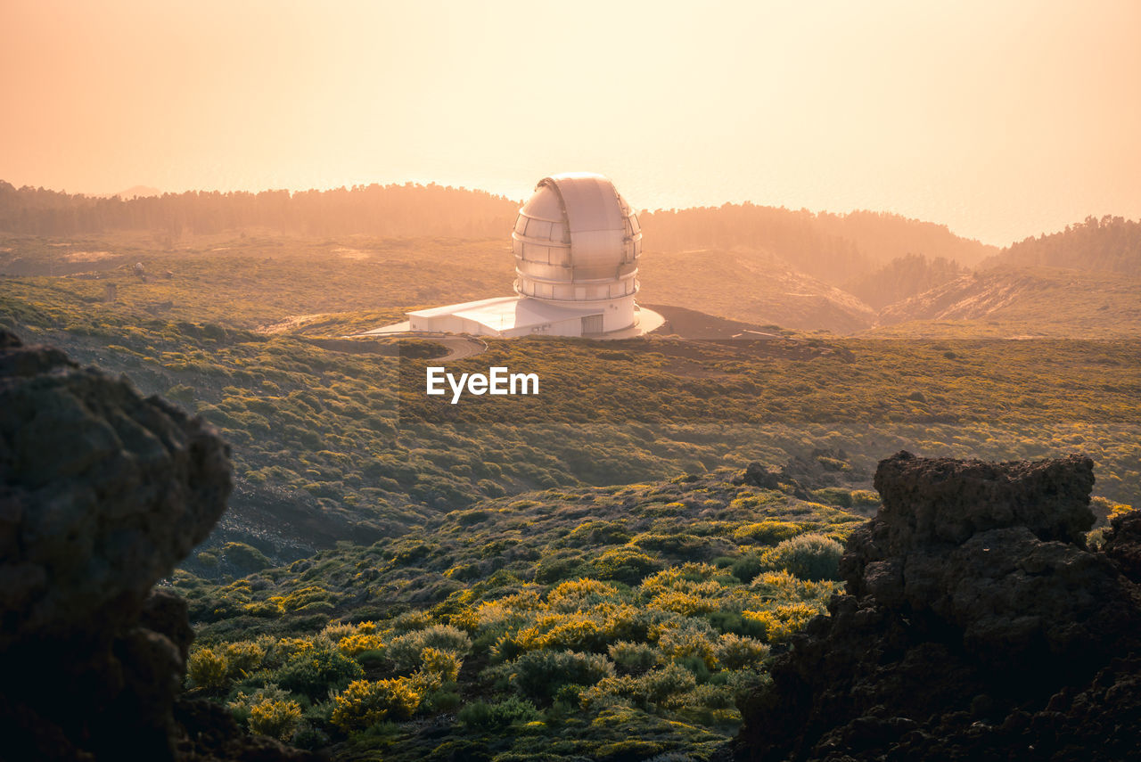 High angle of breathtaking landscape with observatory located on hill above clouds at sunset