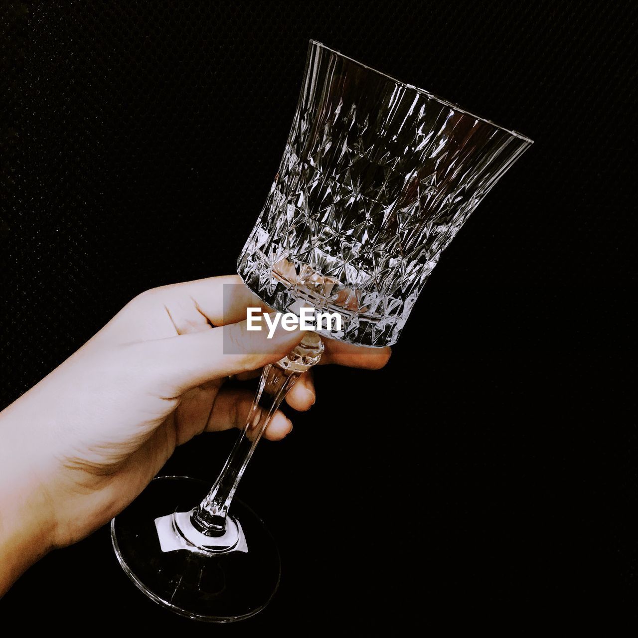 Close-up of hand holding wineglass against black background