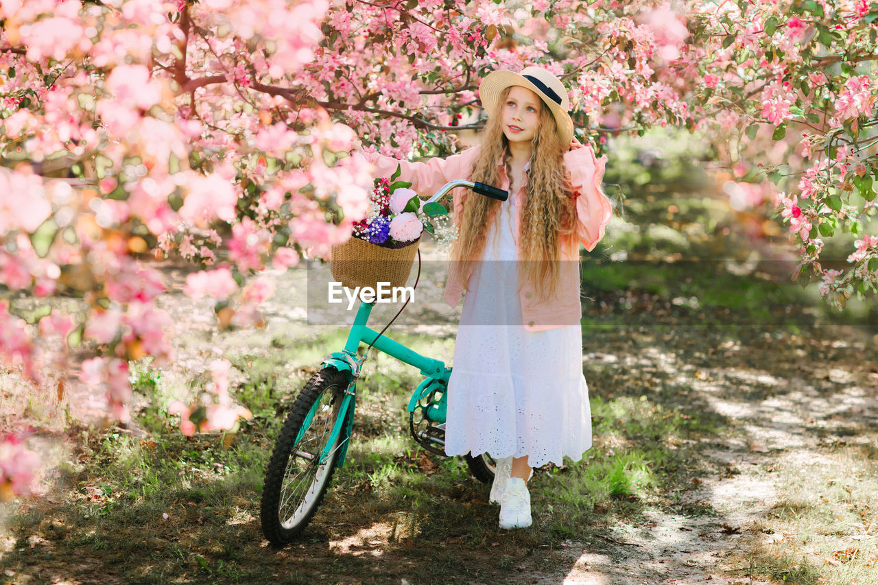 Cute girl with bicycle standing by flowering plant