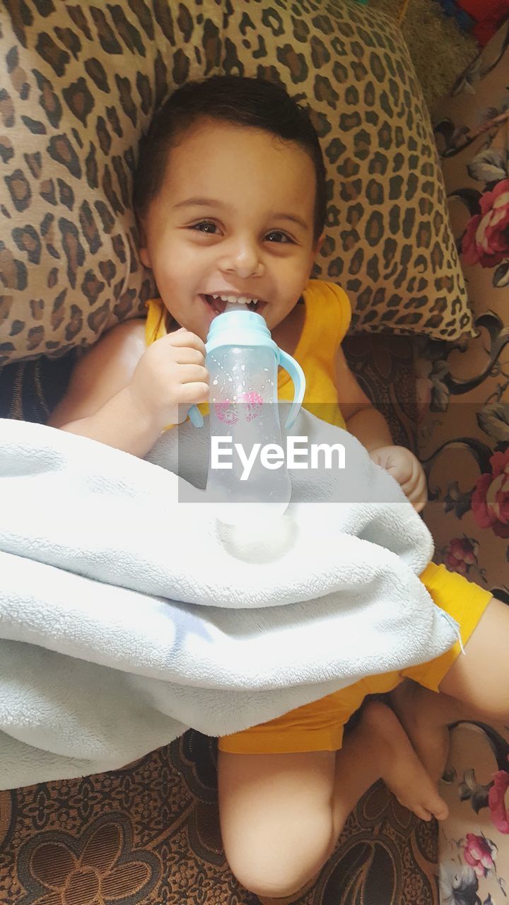 PORTRAIT OF CUTE BOY DRINKING WATER FROM BED