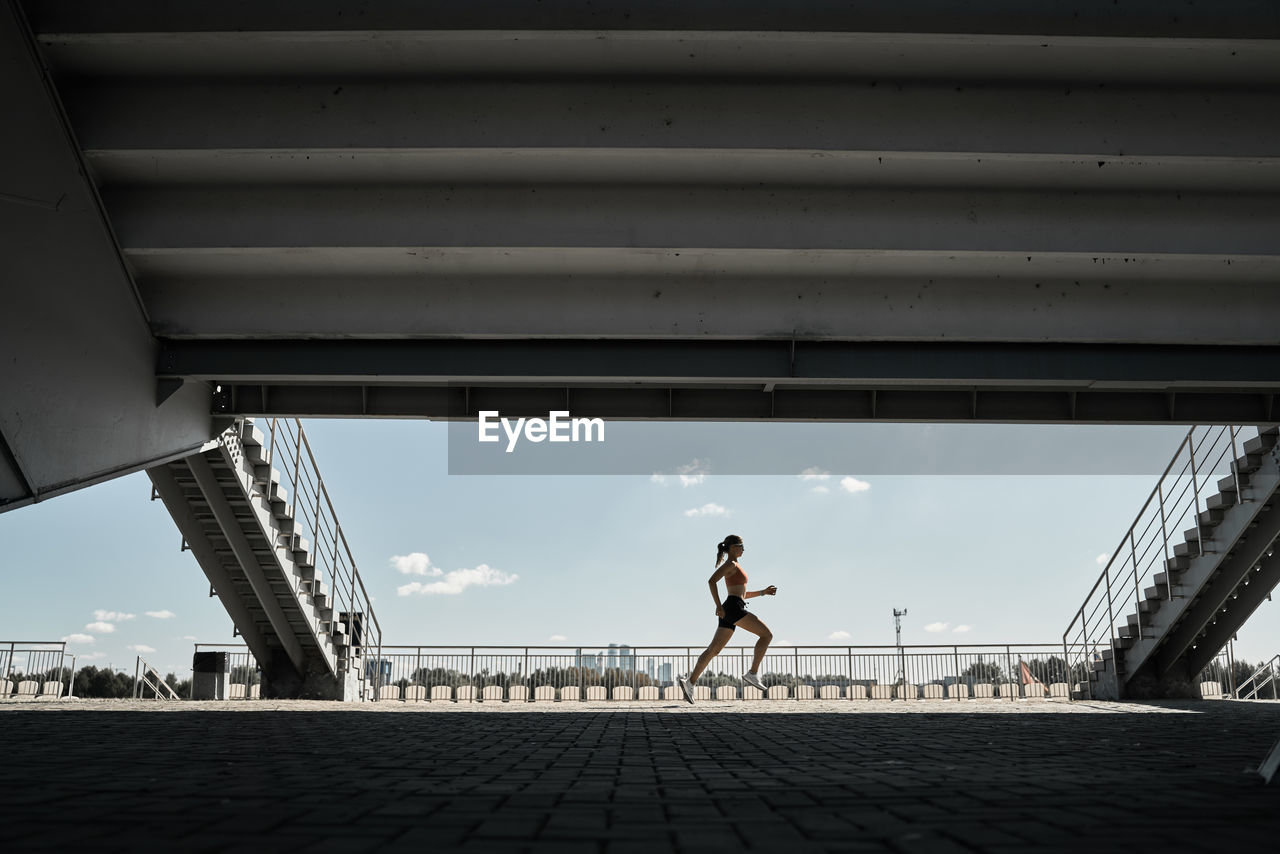 Side view of determined female athlete running fast during outdoor workout near stairways of stadium