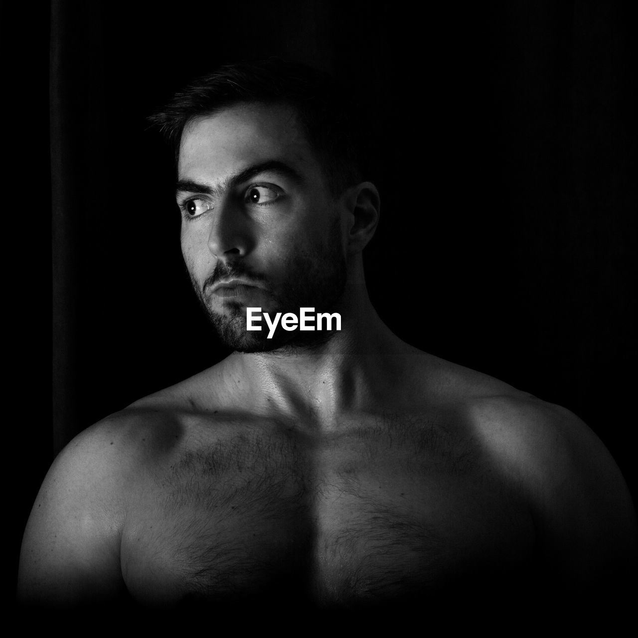 Shirtless young man looking away against black background