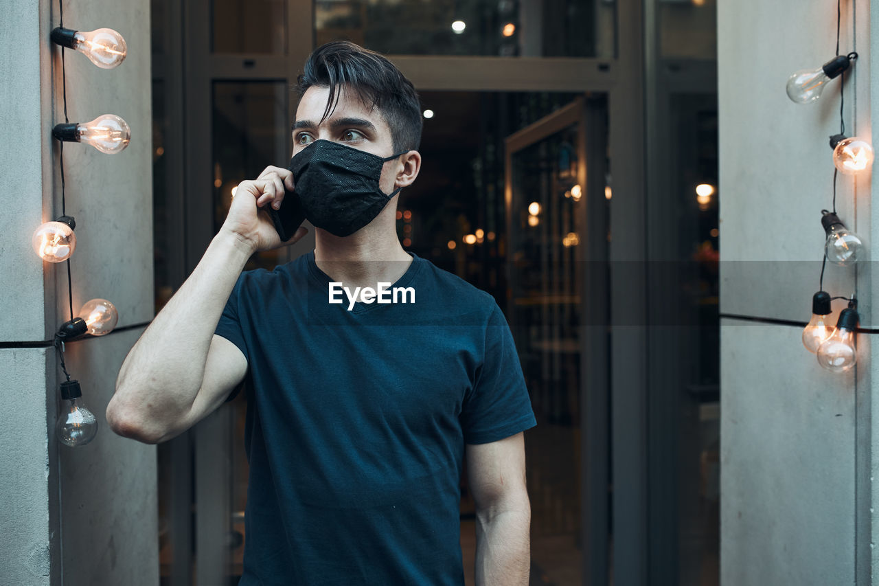 Close-up of young man wearing mask talking on mobile phone outdoors