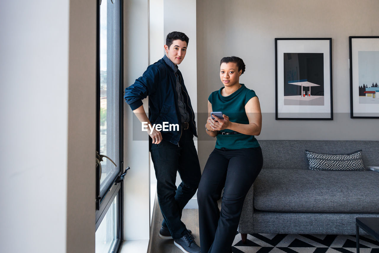 Portrait of businesswoman holding mobile phone while standing with coworker at office