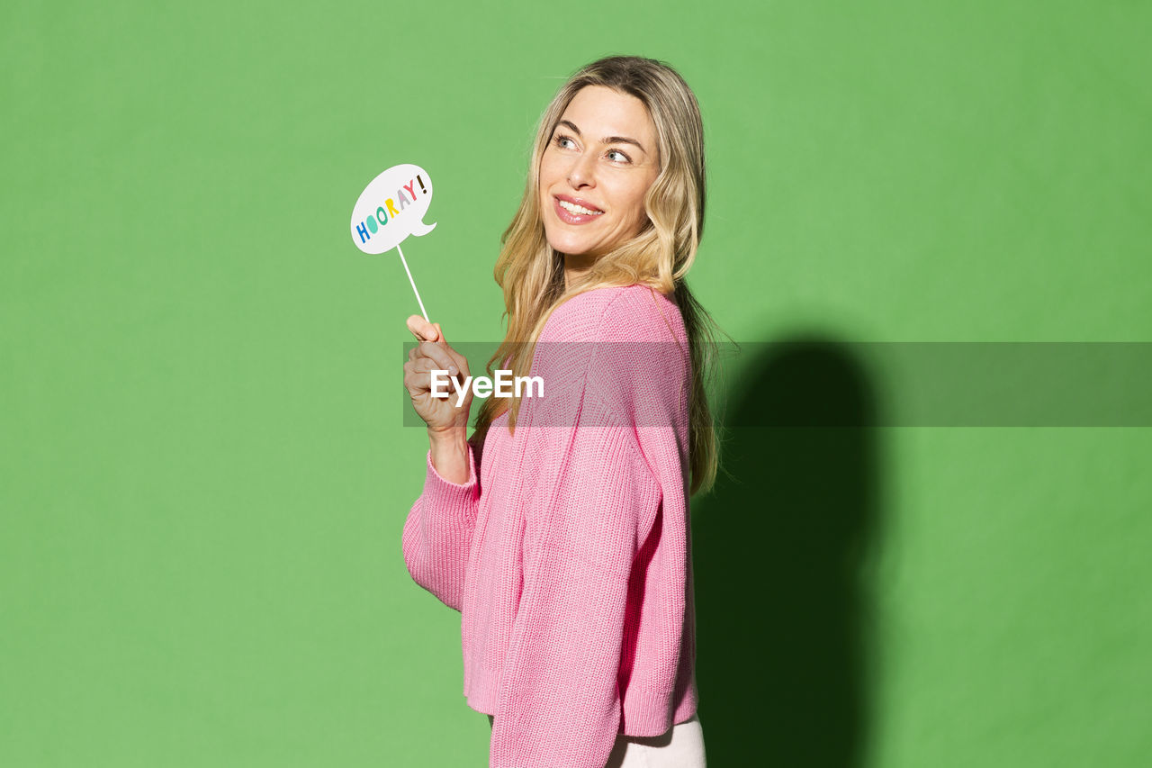 Smiling woman holding speech bubble with hurray text on it against green background