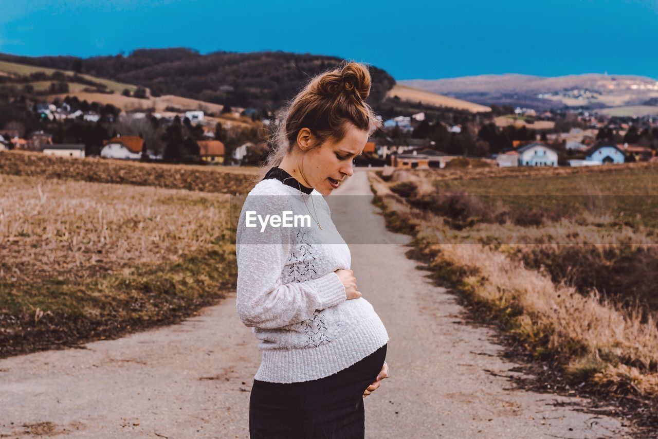Pregnant woman standing on road amidst field