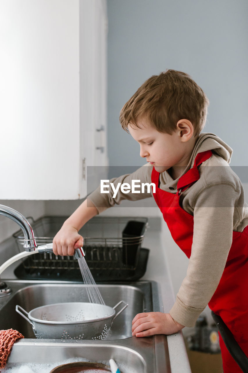 Side view of boy cleaning colander in kitchen sink
