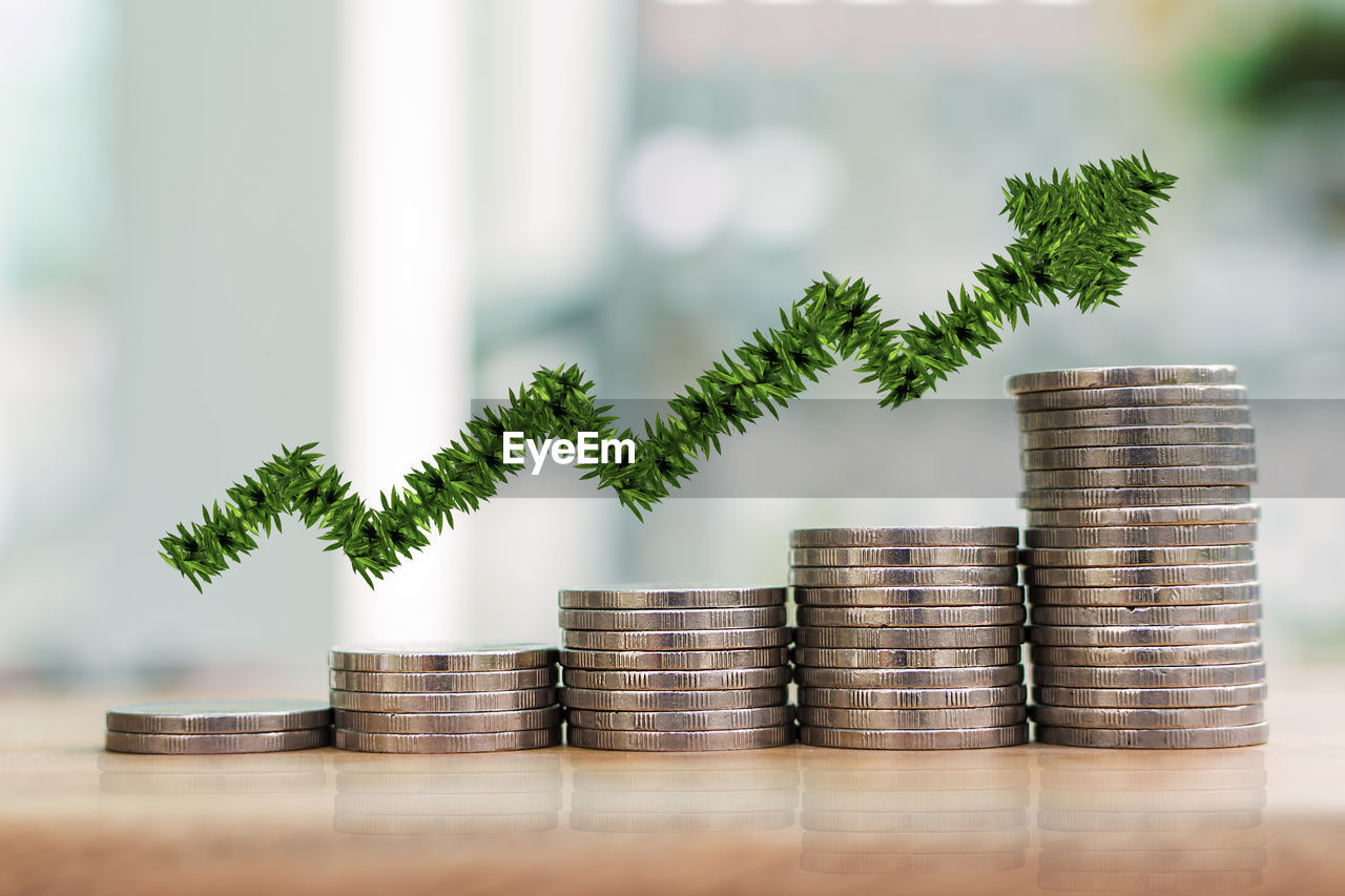 Digital composite image of arrow symbol over coins stacked on table