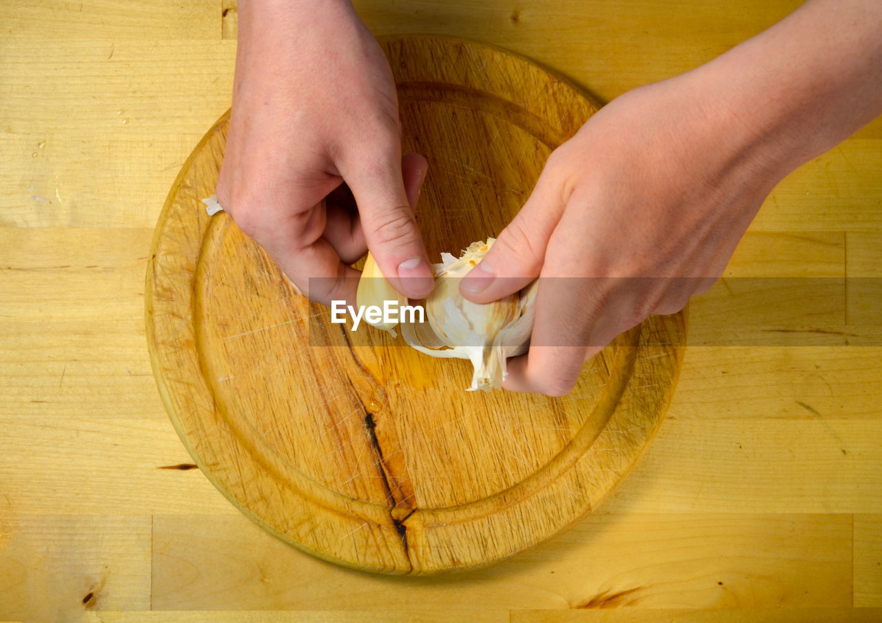 Cropped hands breaking garlic clove over cutting board