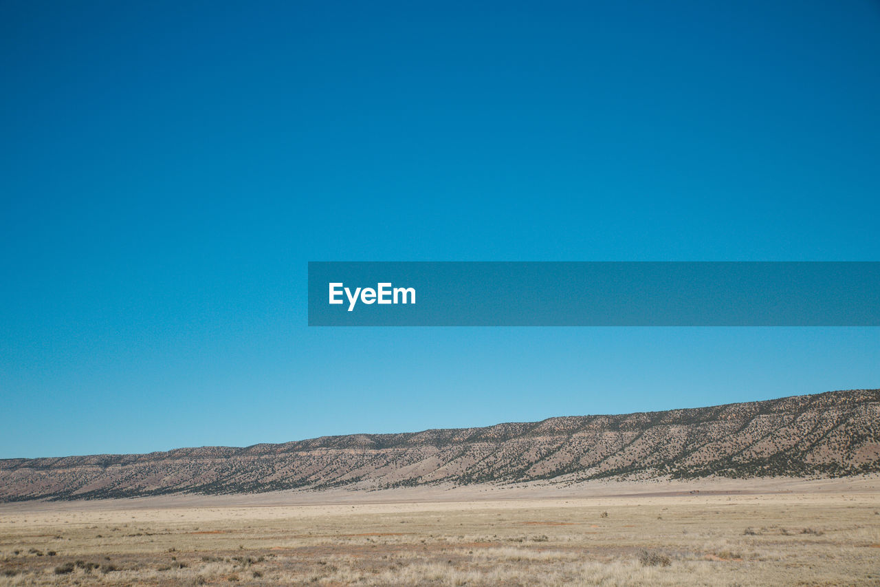 Scenic view of arid landscape against clear blue sky during sunny day