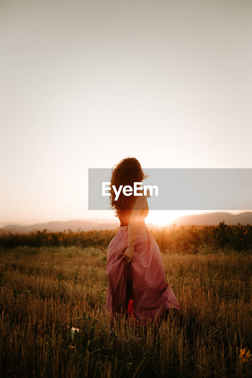 Woman standing on land against clear sky during sunset