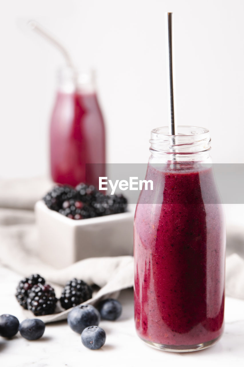 A glass bottle containing pink homemade berry smoothie, with a metal straw to drink it. vertical image.