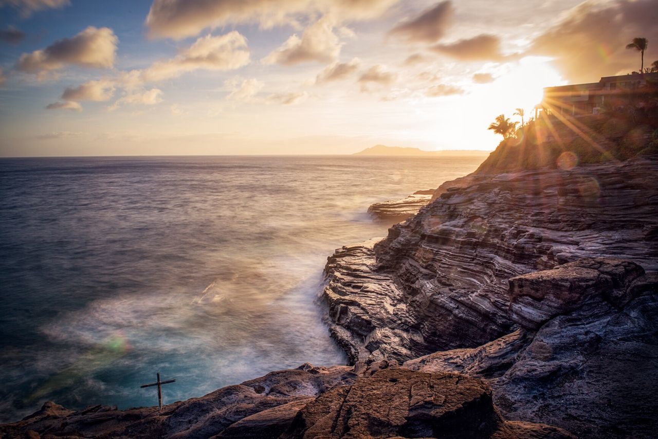 Scenic view of sea and rocky mountains against cloudy sky during sunset
