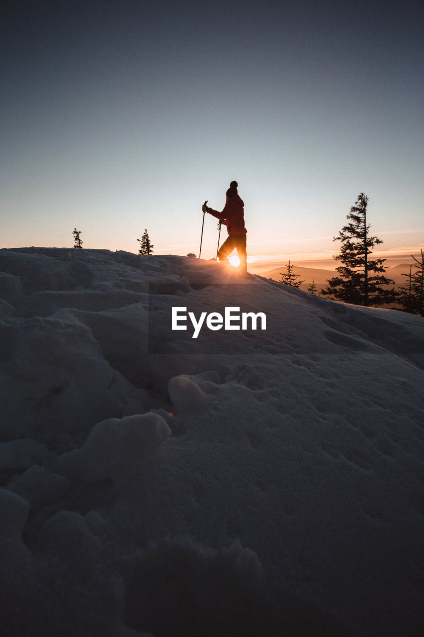 Silhouette woman standing on snow covered mountain during sunset