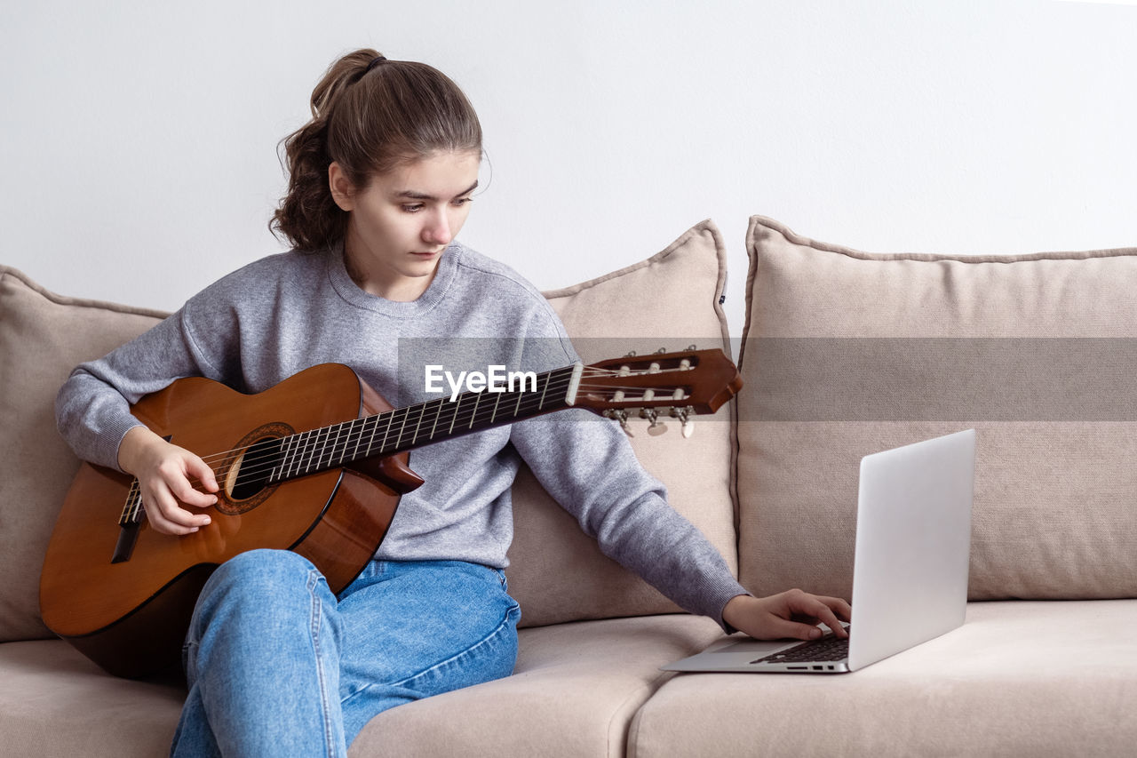 Girl using laptop while playing guitar