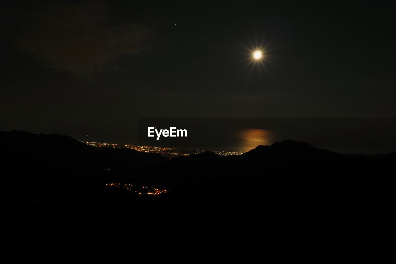 SILHOUETTE OF ILLUMINATED MOUNTAIN AGAINST SKY AT NIGHT