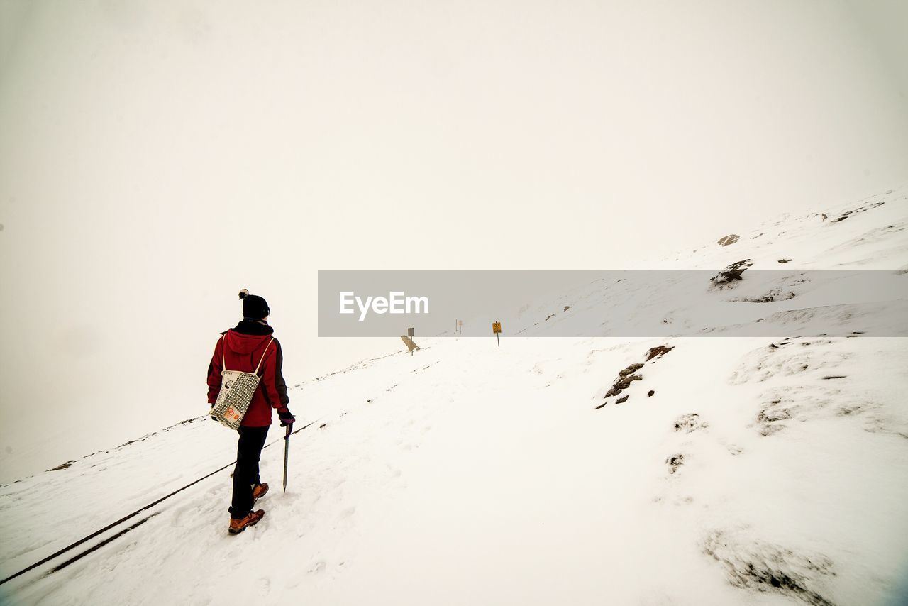 Low angle view of man climbing on snow covered mountain against clear sky