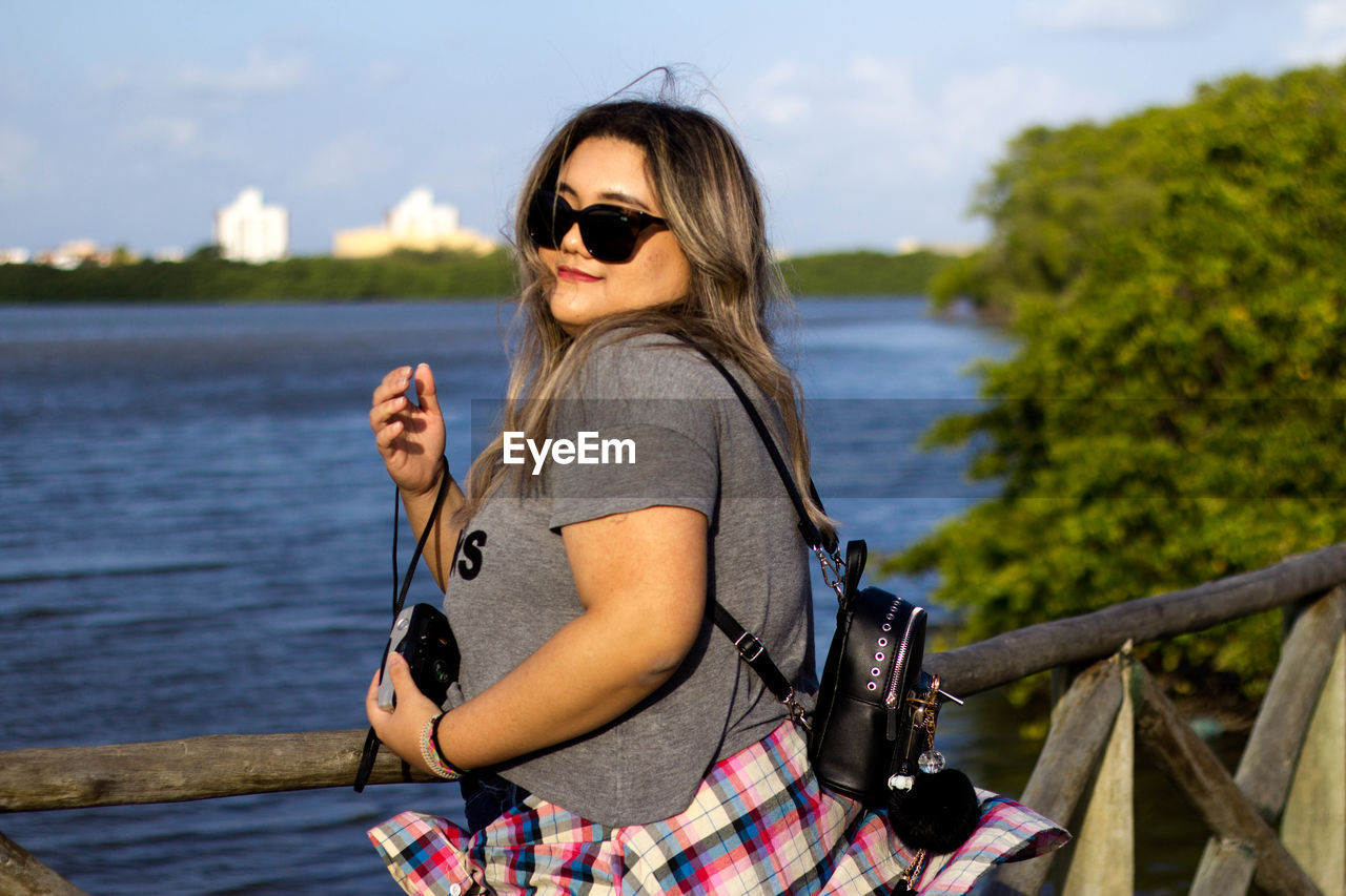 YOUNG WOMAN WEARING SUNGLASSES AGAINST THE SKY