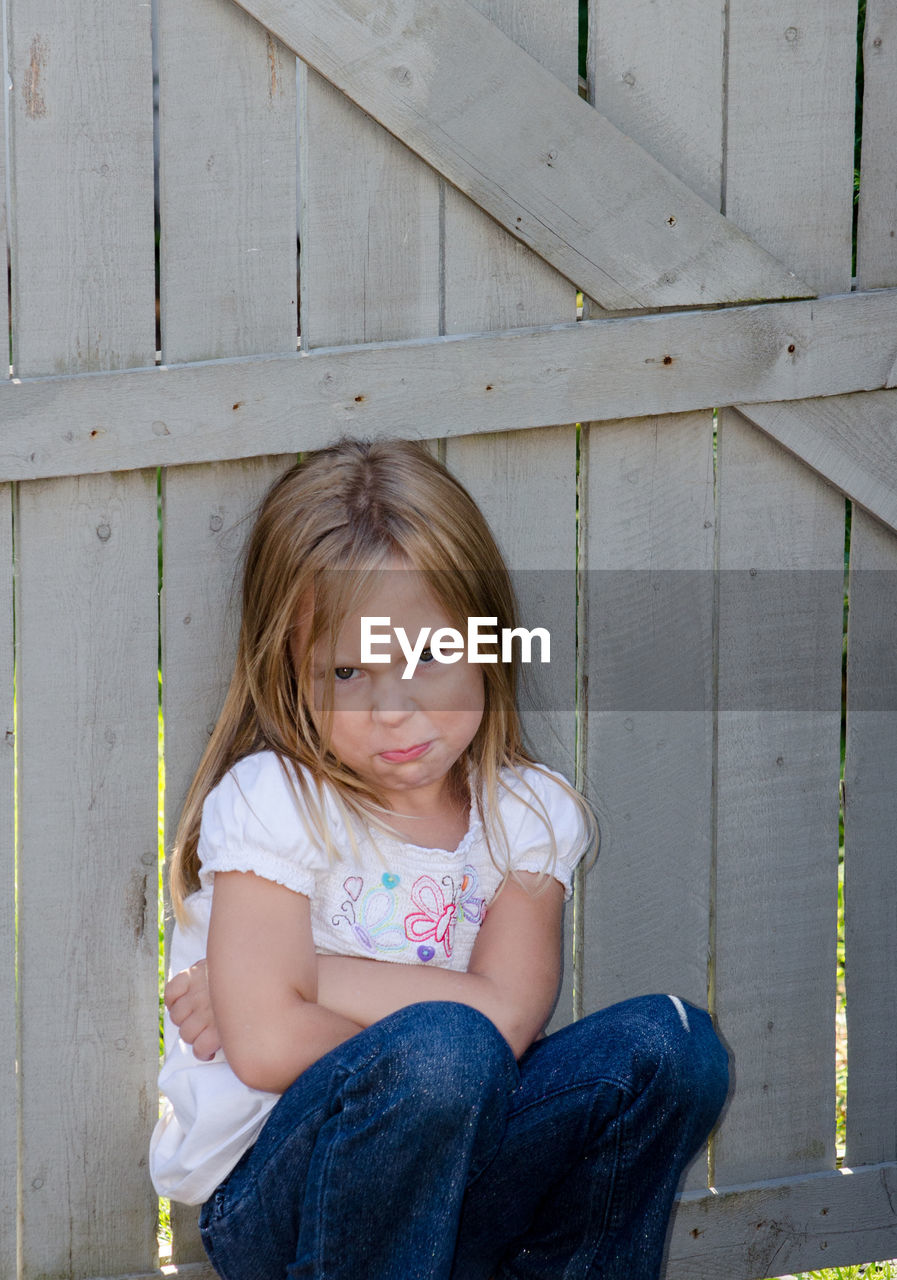 Defiant little girl pouting by a fence