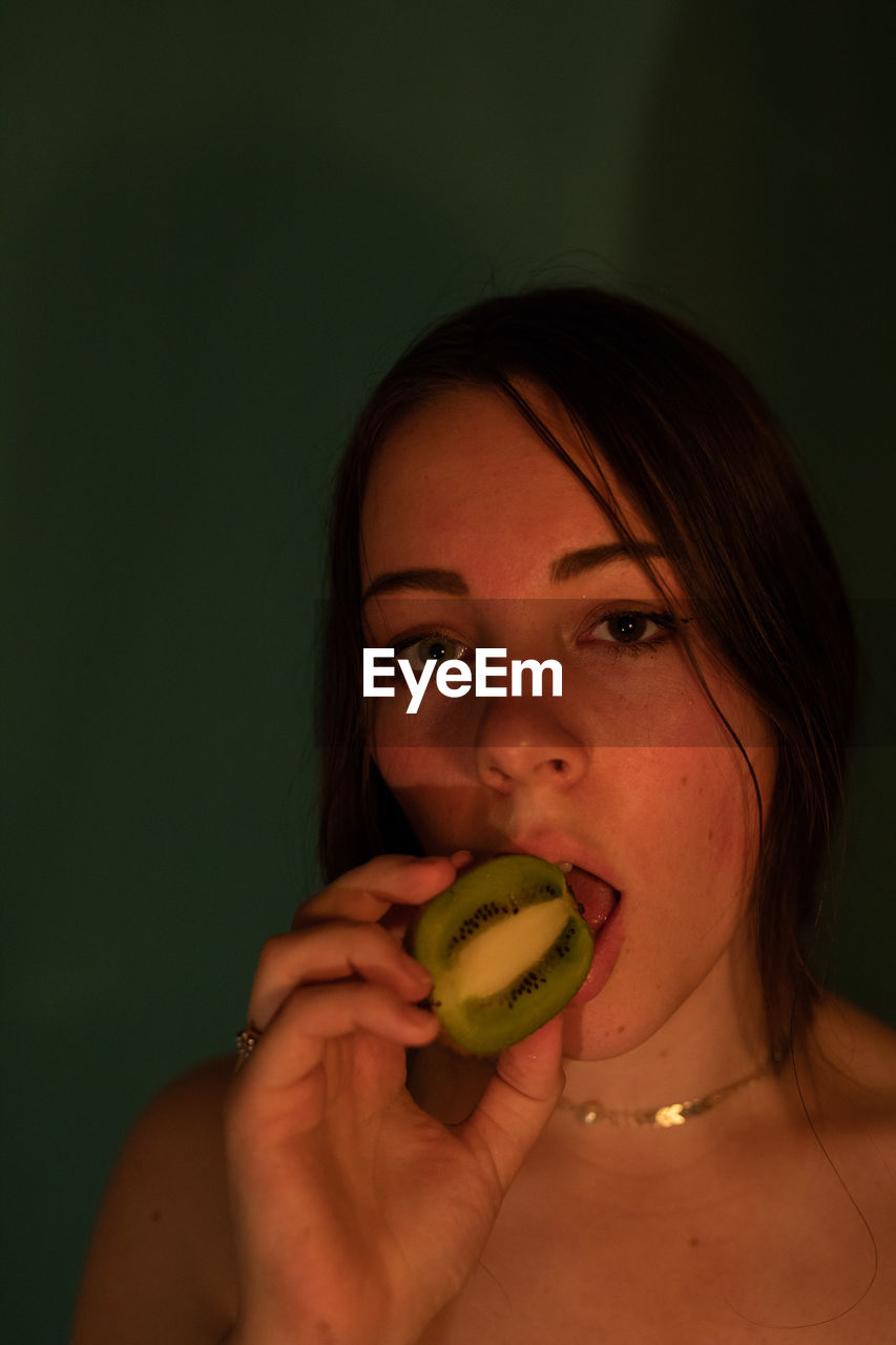 Portrait of woman eating kiwi fruit in darkroom