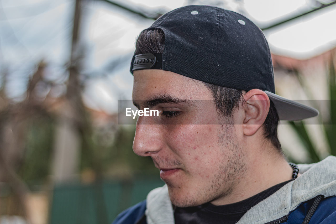 PORTRAIT OF YOUNG MAN LOOKING AWAY OUTDOORS