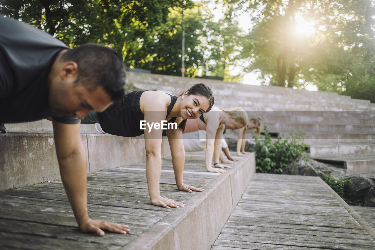 Portrait of smiling woman doing push-ups with friends on steps at park