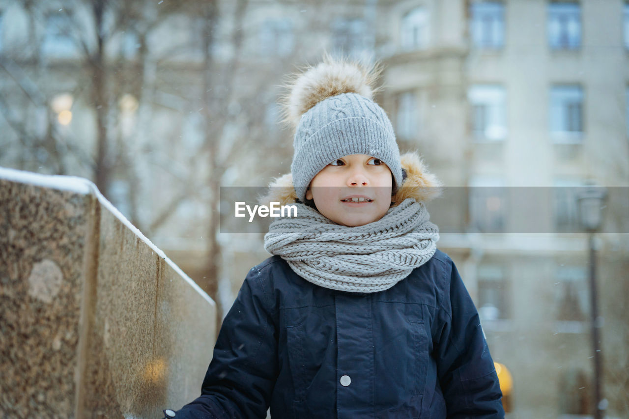 Winter portrait of cute caucasian 7 years old boy in knit hat with pompom in city