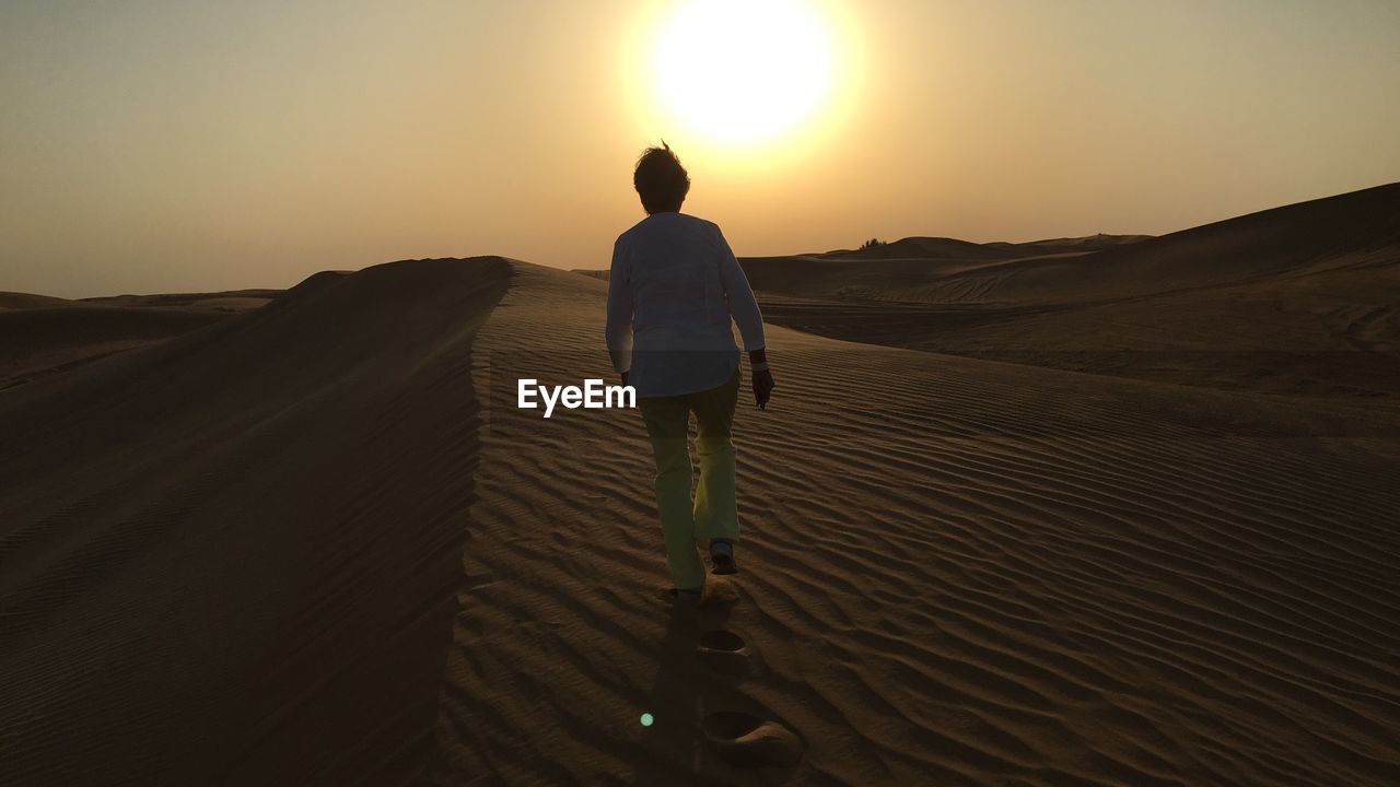 REAR VIEW OF MAN ON SAND IN DESERT AGAINST SKY