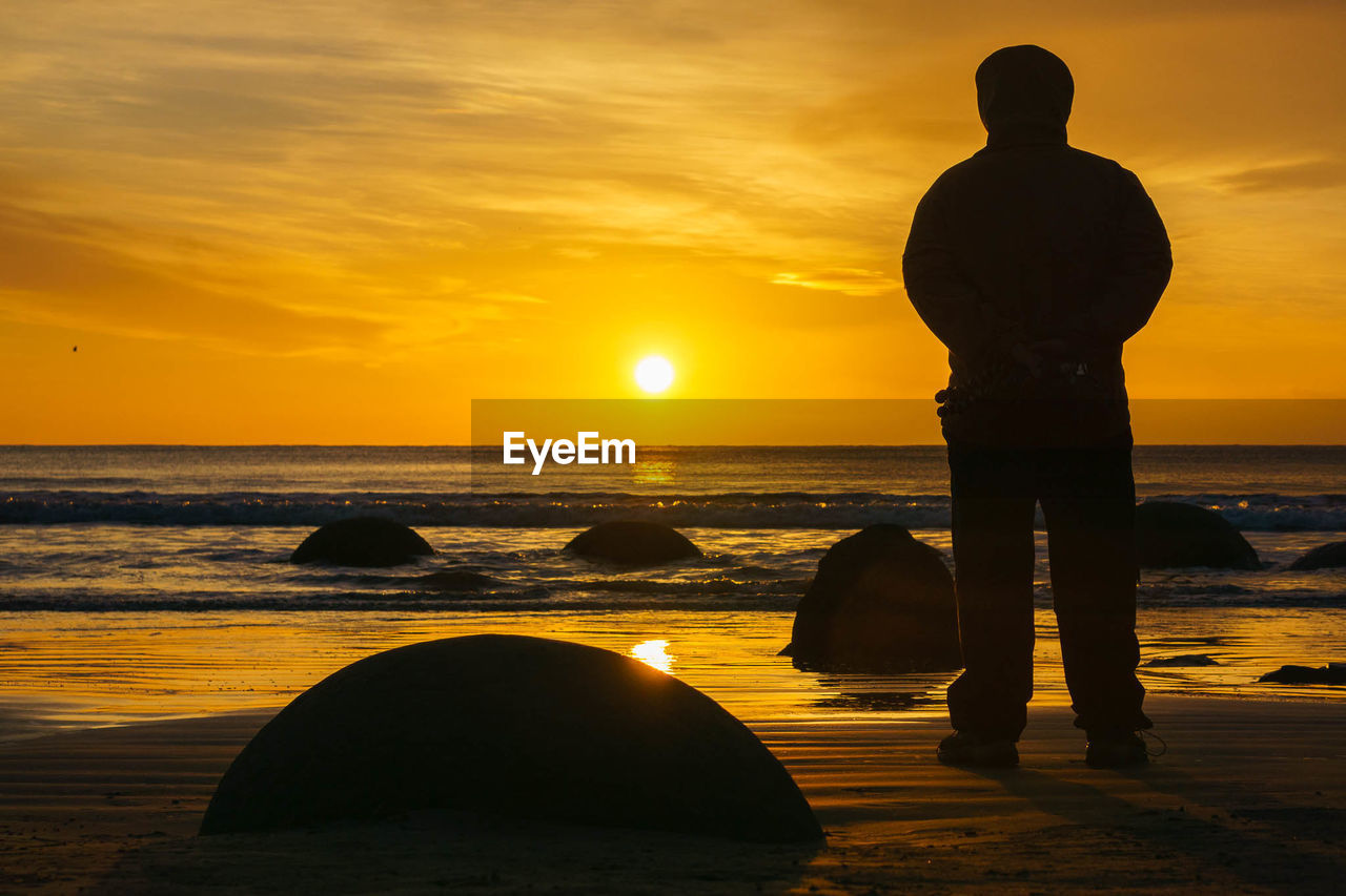 Silhouette man standing at beach against sky during sunset