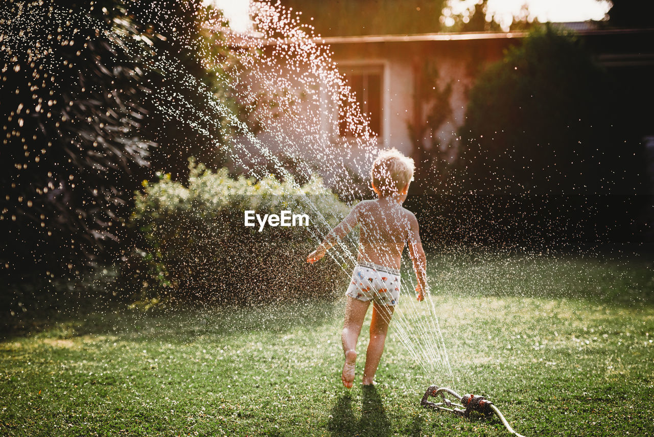 Young child running under the water from the sprinkler in garden