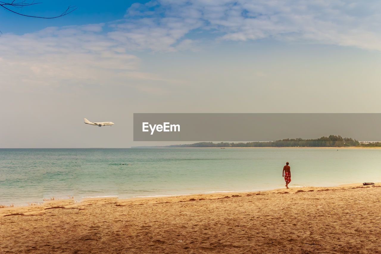 PERSON STANDING ON BEACH AGAINST SKY