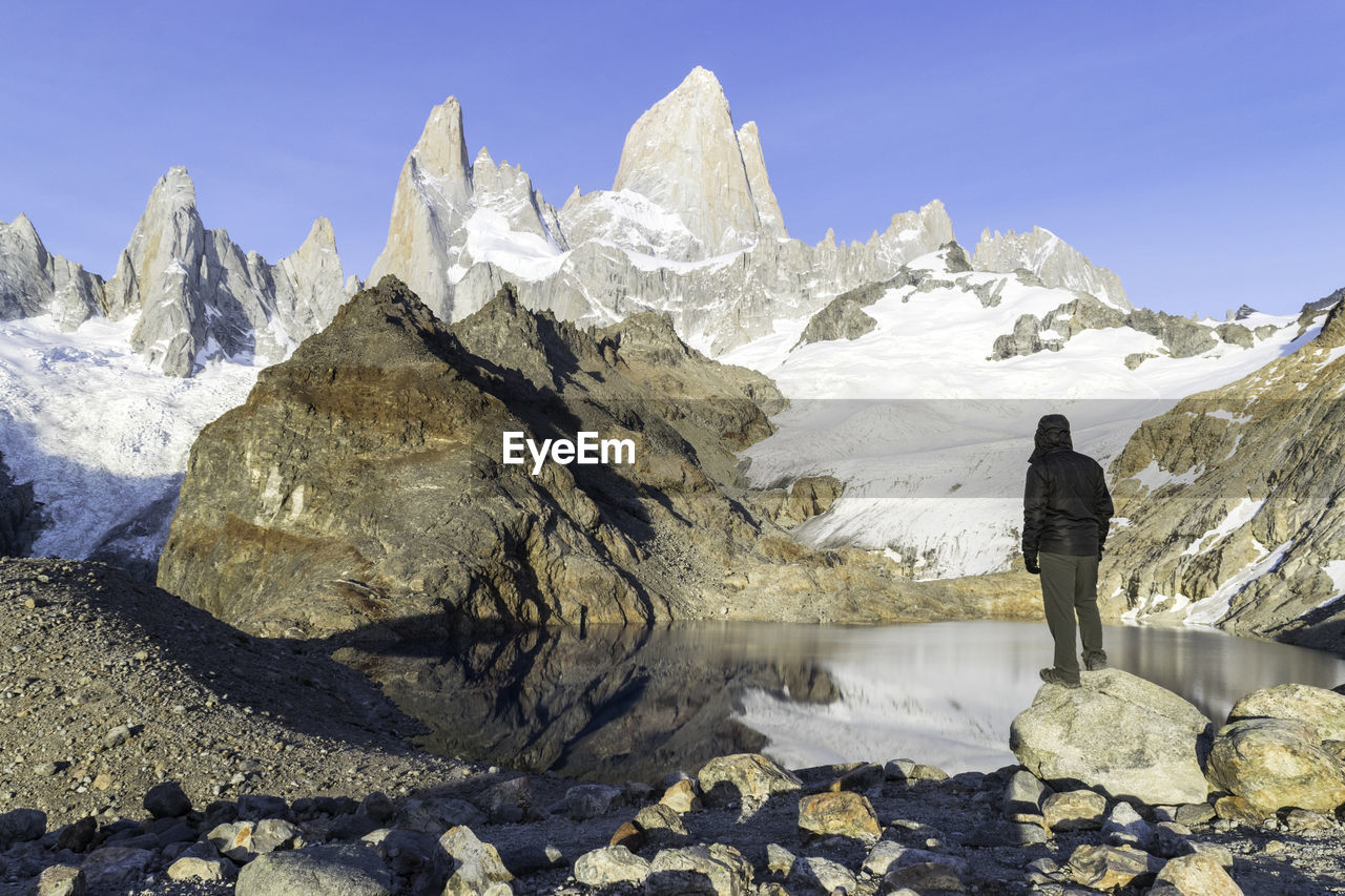 Rear view of person standing on snowcapped mountain against sky