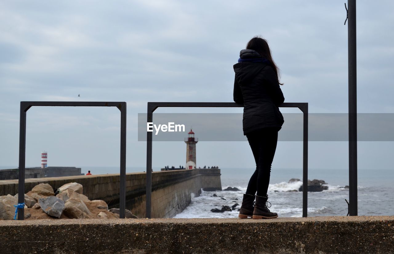 Rear view of woman standing by railing and sea against sky