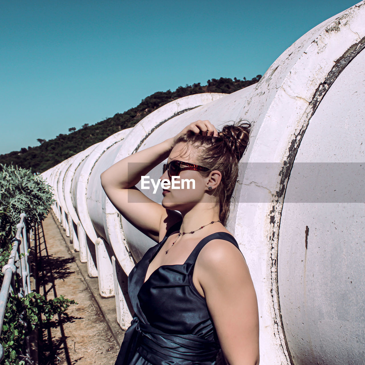 Woman leaning on pipes against clear blue sky