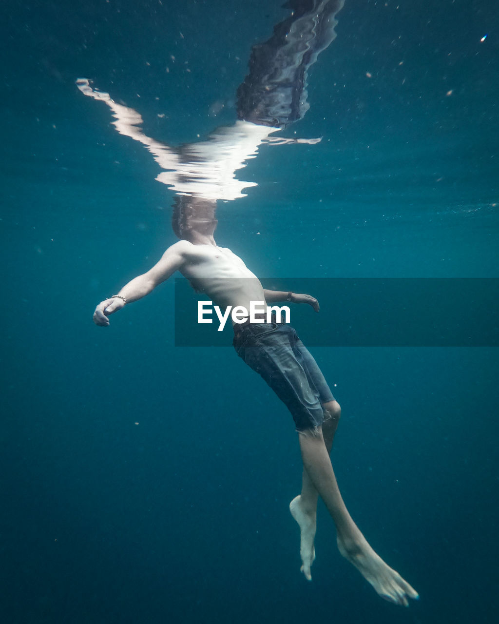 Man wearing short jeans swimming and floating in clear water